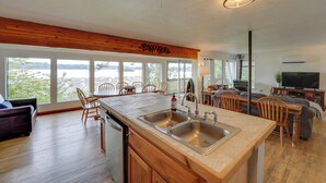 A spacious kitchen with a large island, wooden ceiling, and a view of a lake. - Cozy Beachouse: View & Deck, Steps From Skagit Bay (La Conner)