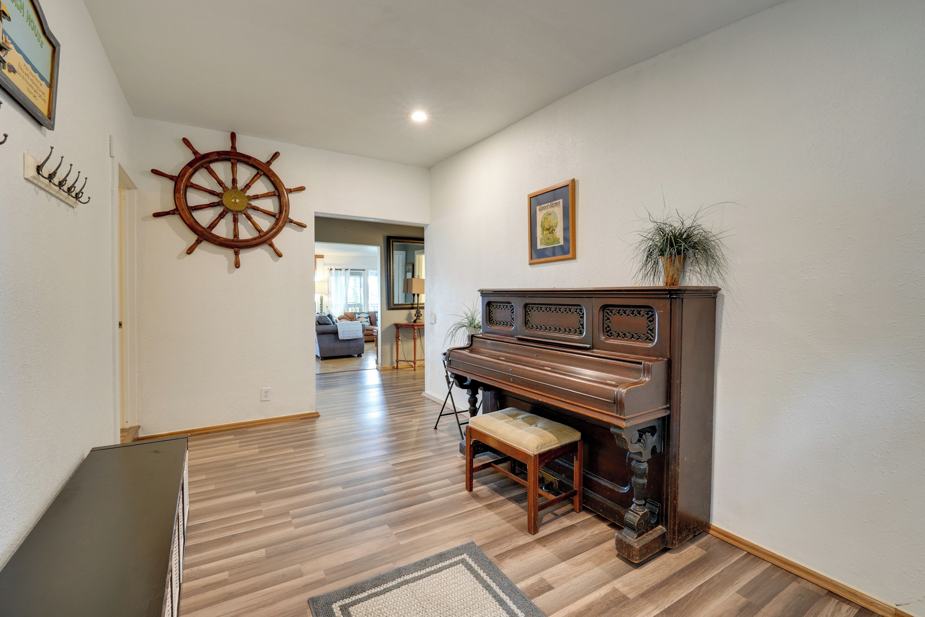 A room with a wooden floor, a piano, a ship's wheel, and a framed picture on the wall.