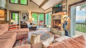 A cozy living room with a fireplace, comfortable seating, and large windows offering a view of the outdoors. - 3 Mi to Beech Mtn: Treetop Cabin w/ Deck & Views (Banner Elk)