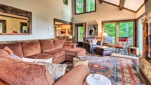 A spacious living room with a large sectional sofa, a coffee table, and a patterned rug. There are multiple windows providing natural light and views of the outdoors. - 3 Mi to Beech Mtn: Treetop Cabin w/ Deck & Views (Banner Elk)