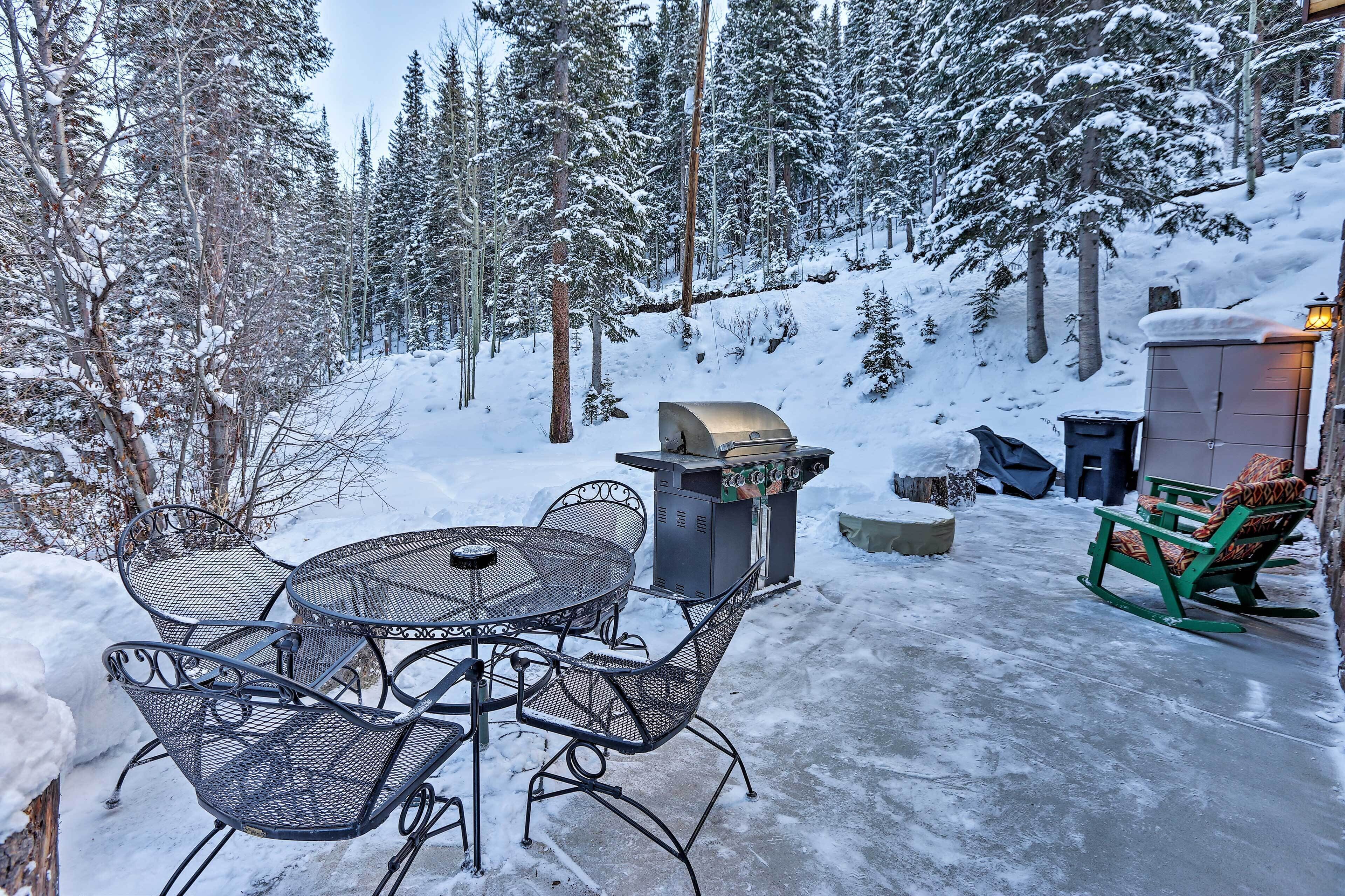 An outdoor patio with metal chairs and a table, surrounded by snow-covered trees.