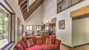 A spacious living area with a large red sectional sofa, wooden beams, and a view of the outdoors. - Cozy Dumont Cottage With Mill Creek Views! (Dumont)