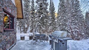A stone building with a red window, a barbecue grill, and a table with chairs in a snowy outdoor area. - Cozy Dumont Cottage With Mill Creek Views! (Dumont)
