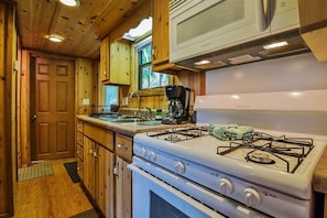 A compact kitchen with wooden cabinets, a gas stove, a microwave, and a coffee maker.