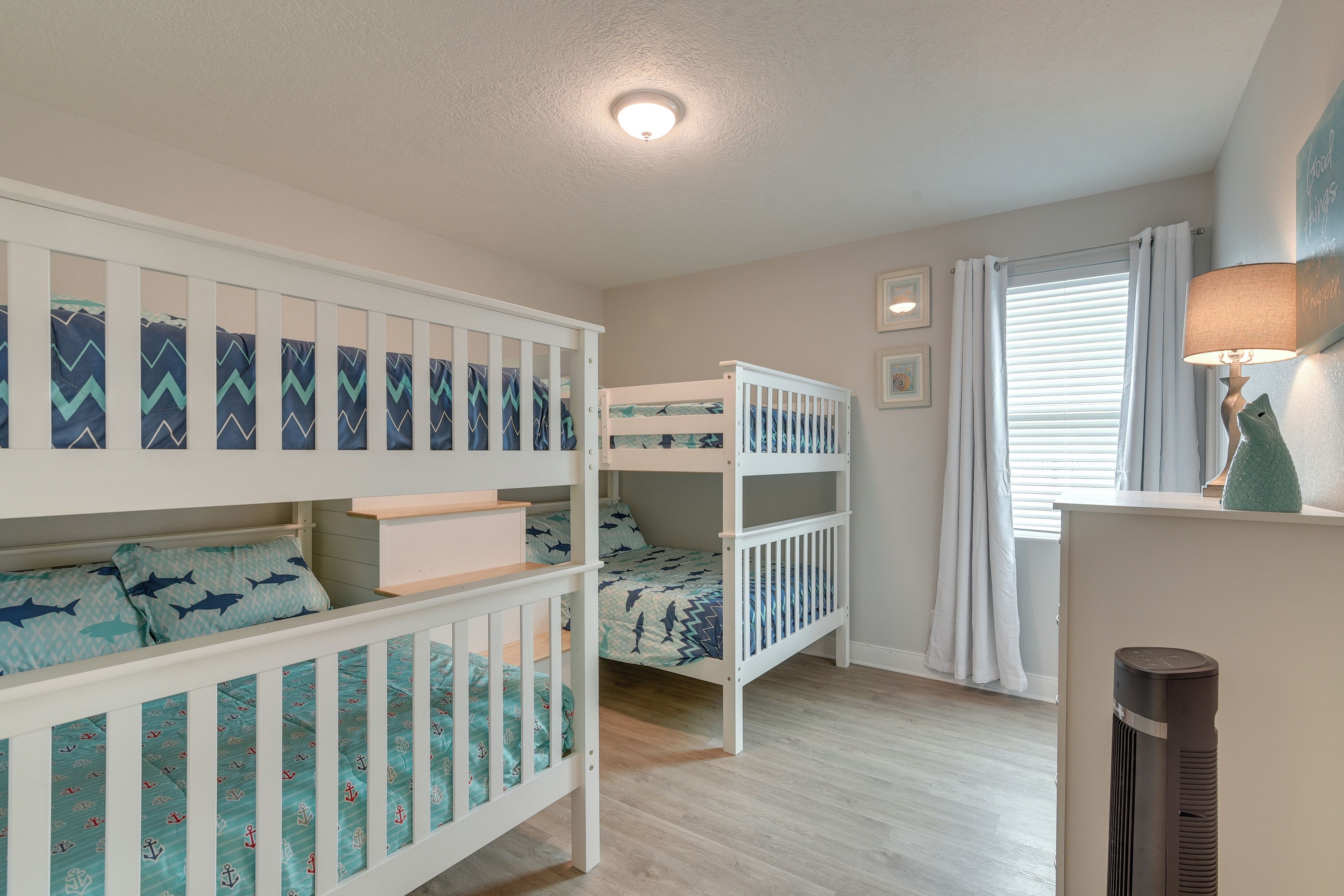 A bedroom with bunk beds, a ceiling light, a window with curtains, and a bedside lamp.