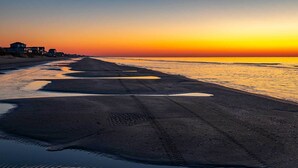 A beach with a sunset, a clear sky, and houses in the background. - Luxe Crystal Beach Retreat w/ Views! Walk to Shore (Port Bolivar)