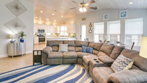 A spacious living room with a large sectional sofa, a ceiling fan, and a kitchen in the background. - Luxe Crystal Beach Retreat w/ Views! Walk to Shore (Port Bolivar)