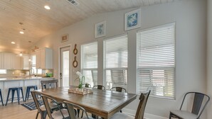 A dining area with a wooden table, six chairs, and a kitchen in the background. - Luxe Crystal Beach Retreat w/ Views! Walk to Shore (Port Bolivar)