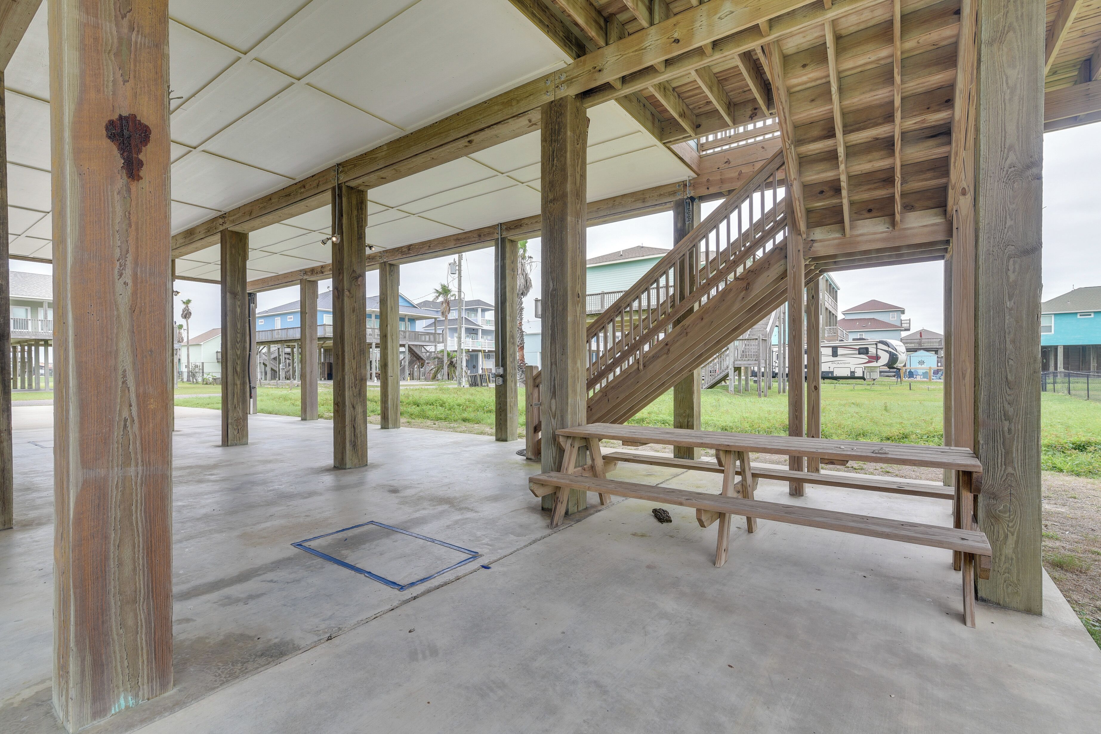 An open wooden structure with a concrete floor, a wooden bench, and a staircase.