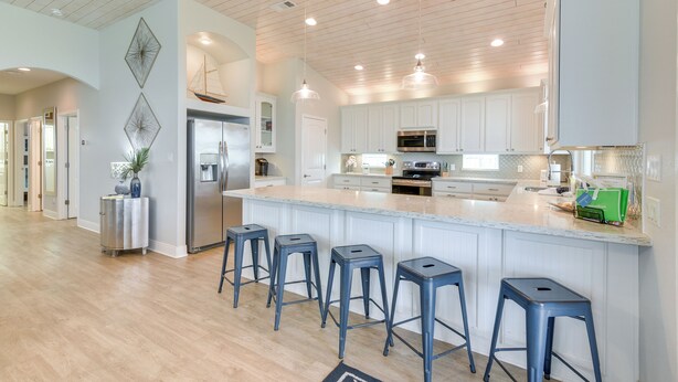 A modern kitchen with white cabinets, a large island with bar stools, stainless steel appliances, and pendant lighting. - Luxe Crystal Beach Retreat w/ Views! Walk to Shore (Port Bolivar)
