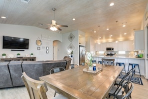 A spacious living room with a large wooden dining table, a comfortable sofa, and a kitchen area with white cabinets and modern appliances. - Luxe Crystal Beach Retreat w/ Views! Walk to Shore (Port Bolivar)