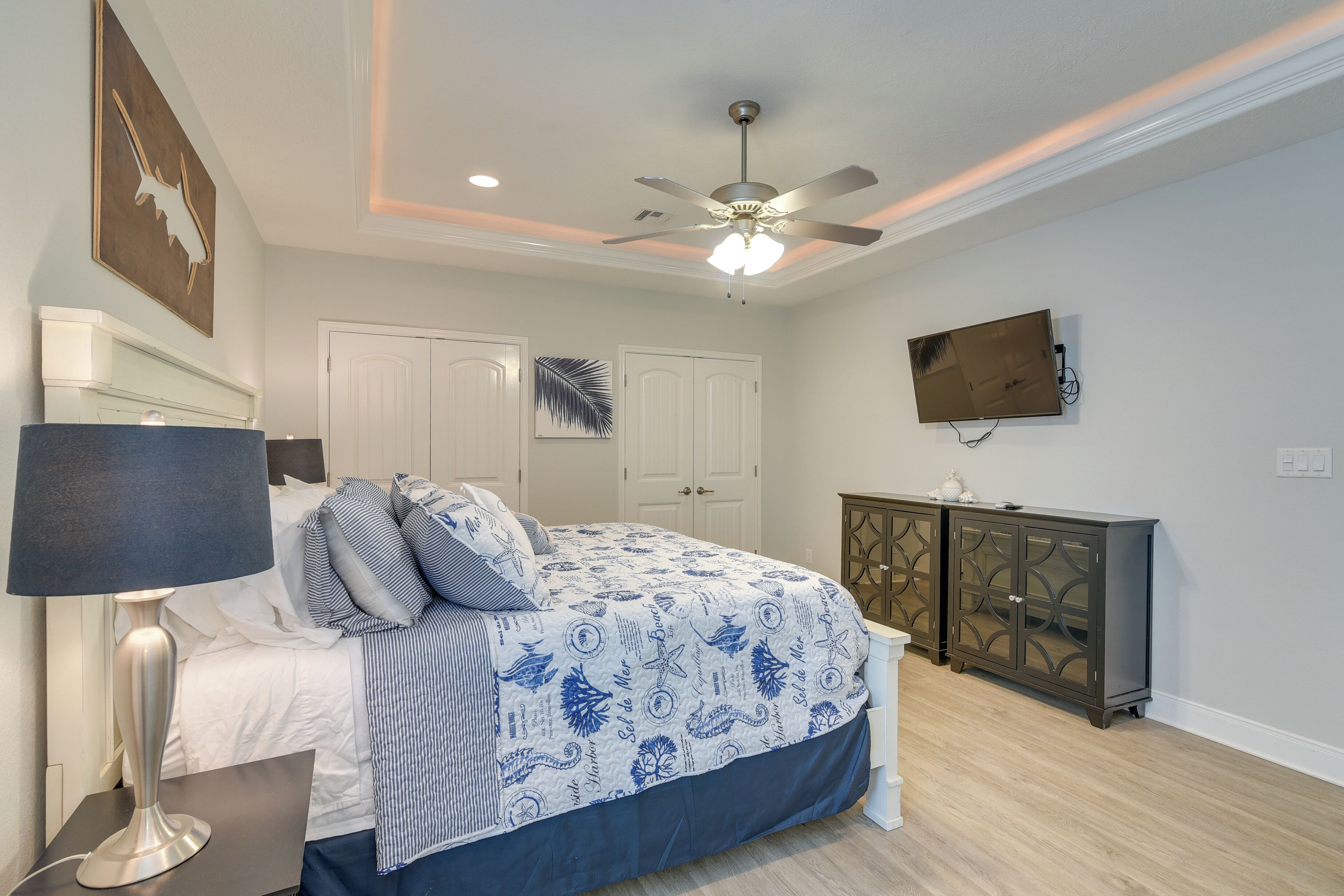 A bedroom with a bed, a ceiling fan, a TV mounted on the wall, and a nightstand with a lamp.