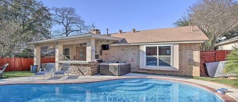 A backyard with a swimming pool, a hot tub, and a covered patio area.