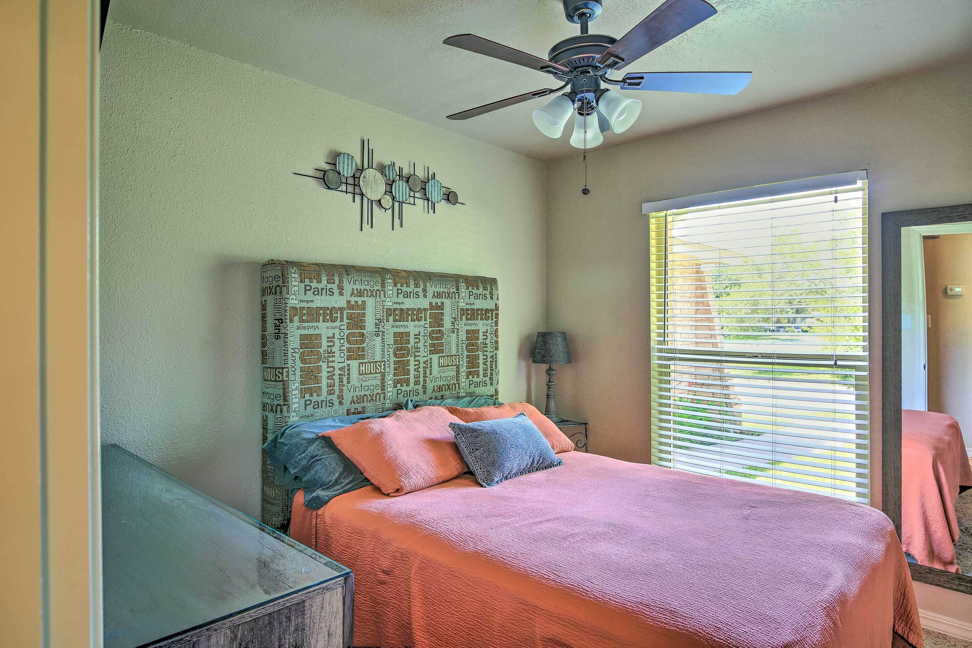 A bedroom with a bed, a ceiling fan, a wall clock, and a window with blinds.