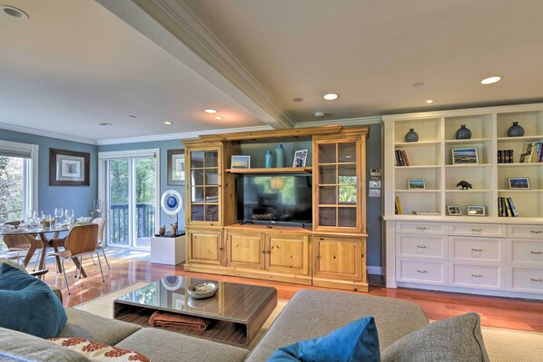 A spacious living room with a wooden entertainment center, a dining area with a glass door, and a white shelving unit with decorative items. - Designer Apartment < 1 Mile to Downtown San Rafael (San Rafael)