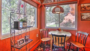 A dining area with a table and chairs, a window with a view of trees, and a decorative shelf with items. - Colorful Bungalow By Pikes Peak/garden of the Gods (Manitou Springs)