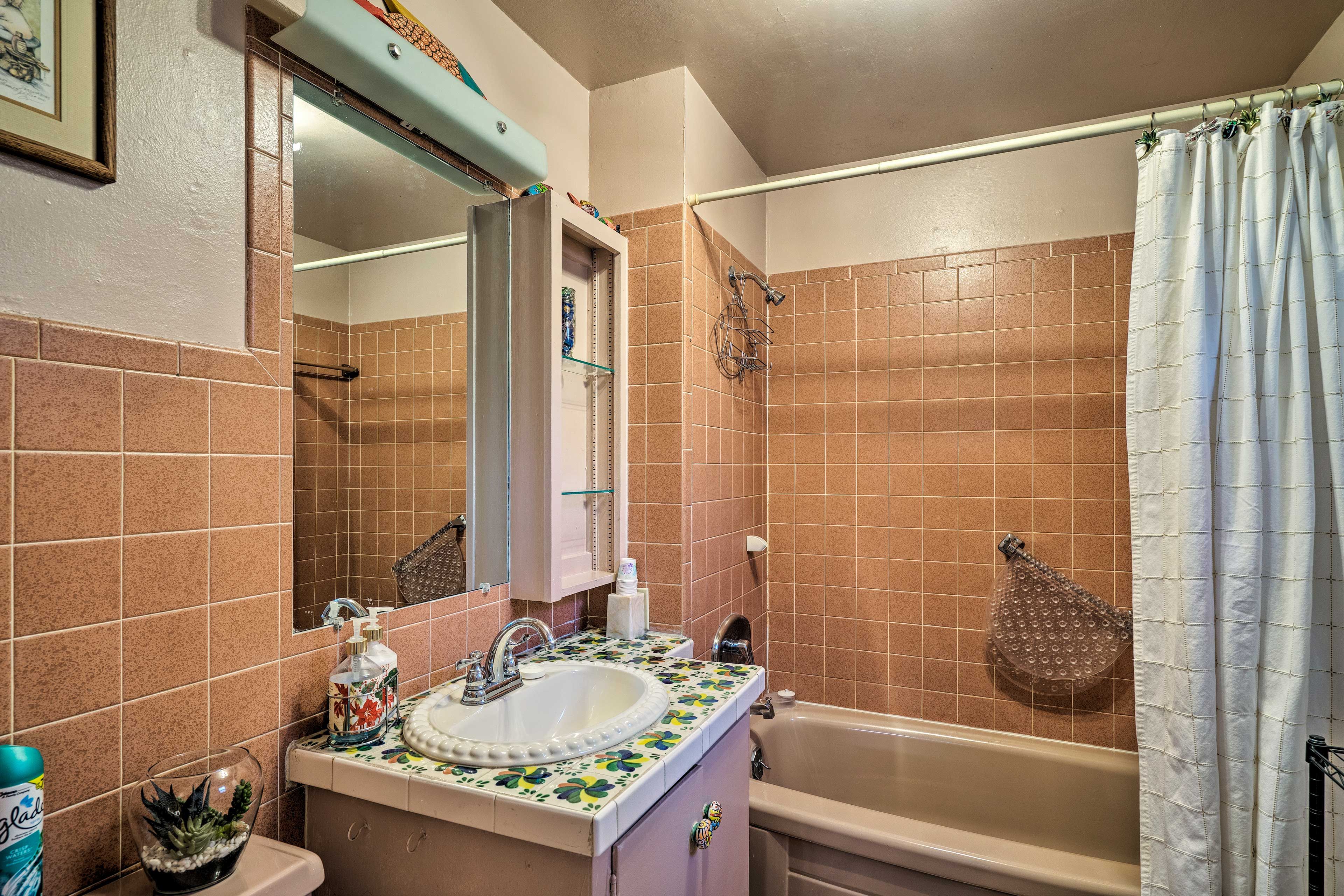 A bathroom with a bathtub, a sink with a decorative tile backsplash, a mirror, and a shower curtain.