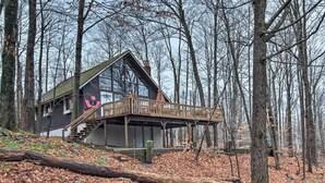 A cabin with a wooden deck and stairs leading to a second-story balcony, surrounded by a forest. - Fire Pit + Community Perks: Gouldsboro Cabin! (Gouldsboro)