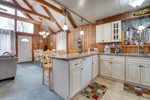 Una cocina con armarios de madera, una zona de comedor con sillas y un ventanal grande.