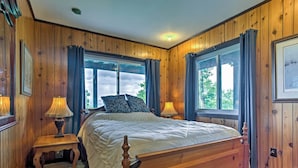 A wooden-paneled bedroom with a large bed, two bedside tables with lamps, and a window with curtains. - Secluded Mountain Home w/ Stunning Views & Deck! (Bryson City)