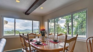 A dining area with a wooden table set for four, surrounded by wooden chairs, large windows with a mountain view, and a blue carpet. - Secluded Mountain Home w/ Stunning Views & Deck! (Bryson City)