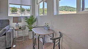 A cozy room with a grey sofa, a small round table with a lamp, a potted plant, and a view of a hilly landscape through large windows. - Cottage by the Lakes w/ Patio by Lake Nacimiento (Bradley)