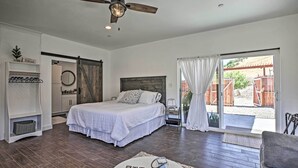 A bedroom with a bed, a ceiling fan, a window with curtains, a small table with a lamp, and a view of the outside. - Cottage by the Lakes w/ Patio by Lake Nacimiento (Bradley)