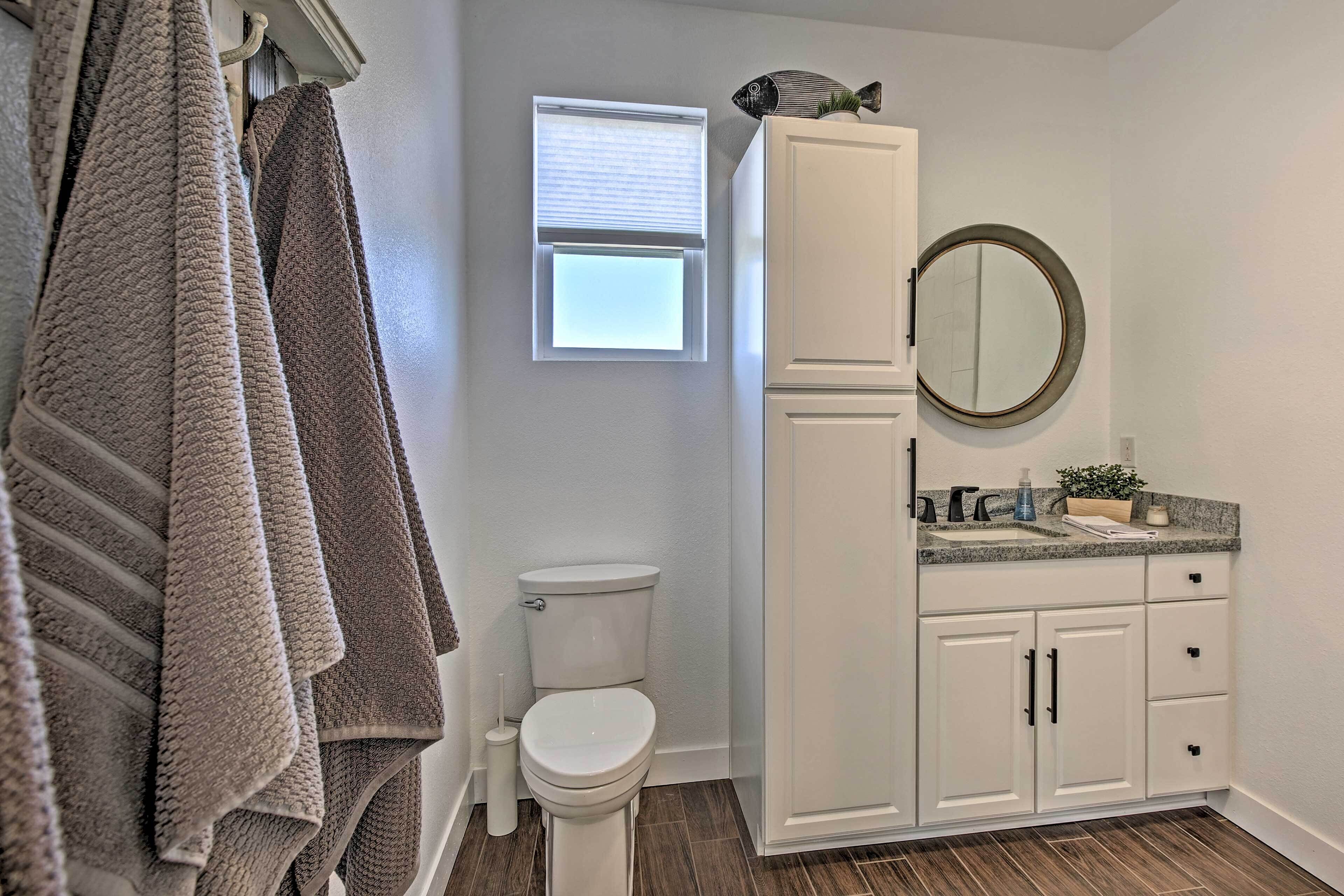 Une salle de bain avec des toilettes, une fenêtre, un lavabo avec un miroir et des serviettes suspendues sur un porte-serviettes.