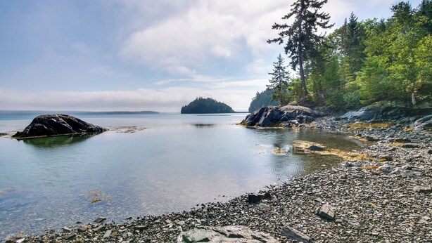 A rocky shoreline with calm water, a forested island in the distance, and a clear sky. - Enchanting Waterfront Sorrento Home w/ Deck! (Sorrento)