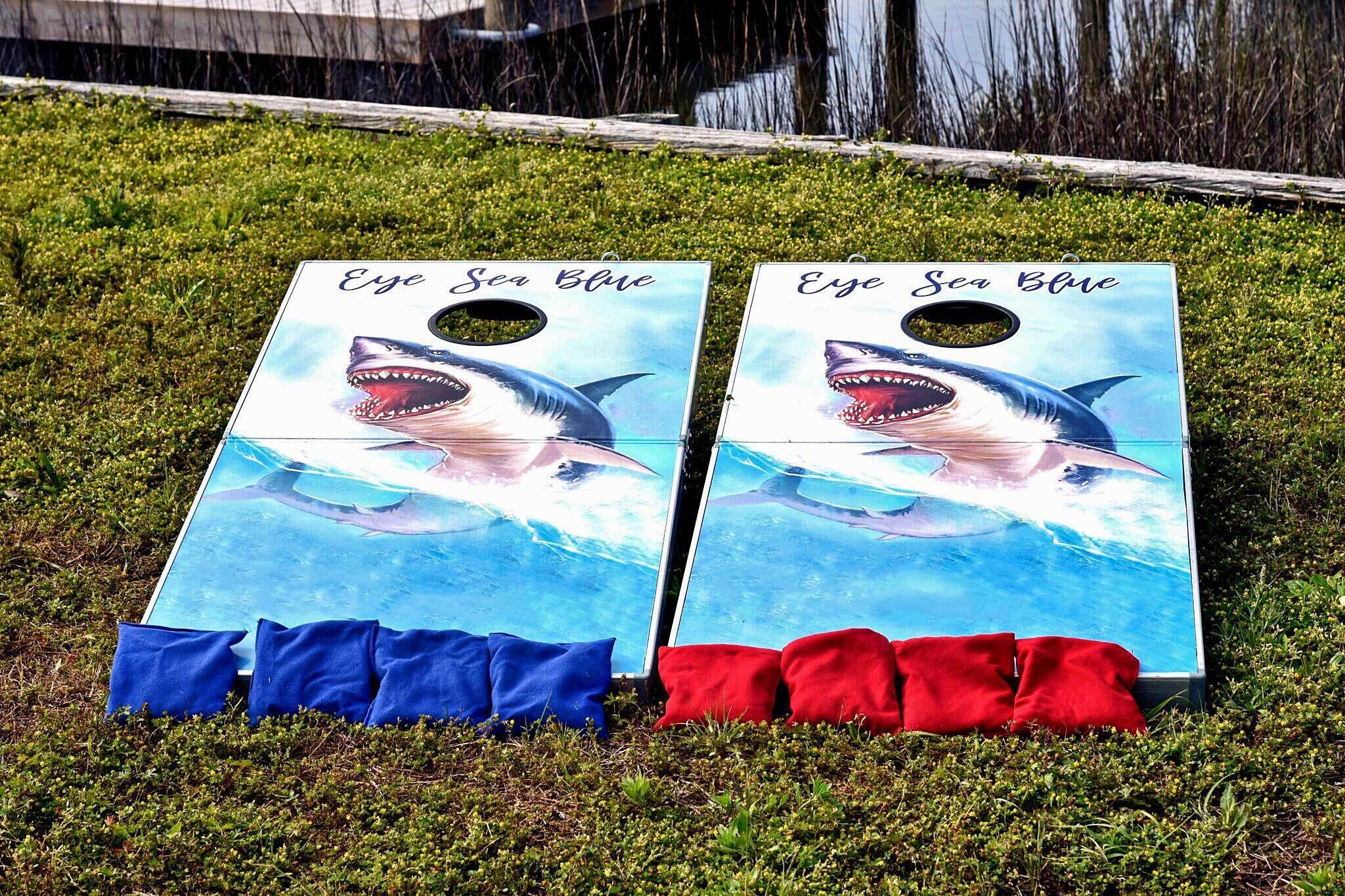 Deux plateaux de jeu intitulés « Eye Sea Blue », ornés de motifs de requins, sont posés sur l’herbe.