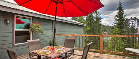 A deck with a table set for four, surrounded by chairs, and a large red umbrella providing shade.