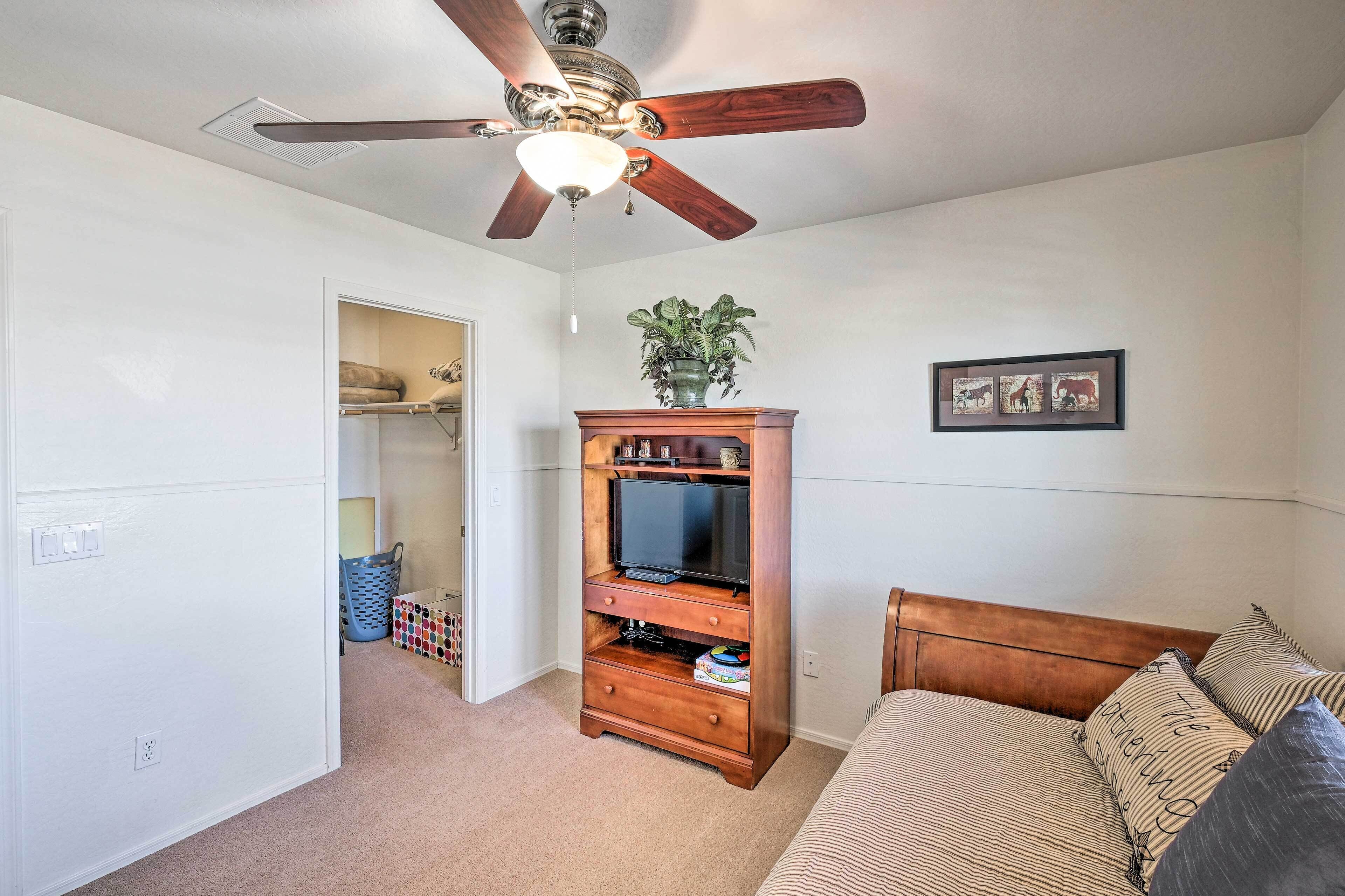 A bedroom with a bed, a wooden dresser, a ceiling fan, a TV, and a plant.