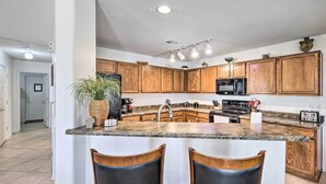 A kitchen with wooden cabinets, a granite countertop, a microwave, and a sink. There are two bar stools and a potted plant. - 'bella Casa' Coolidge Home w/ Pool & Hot Tub! (Coolidge)
