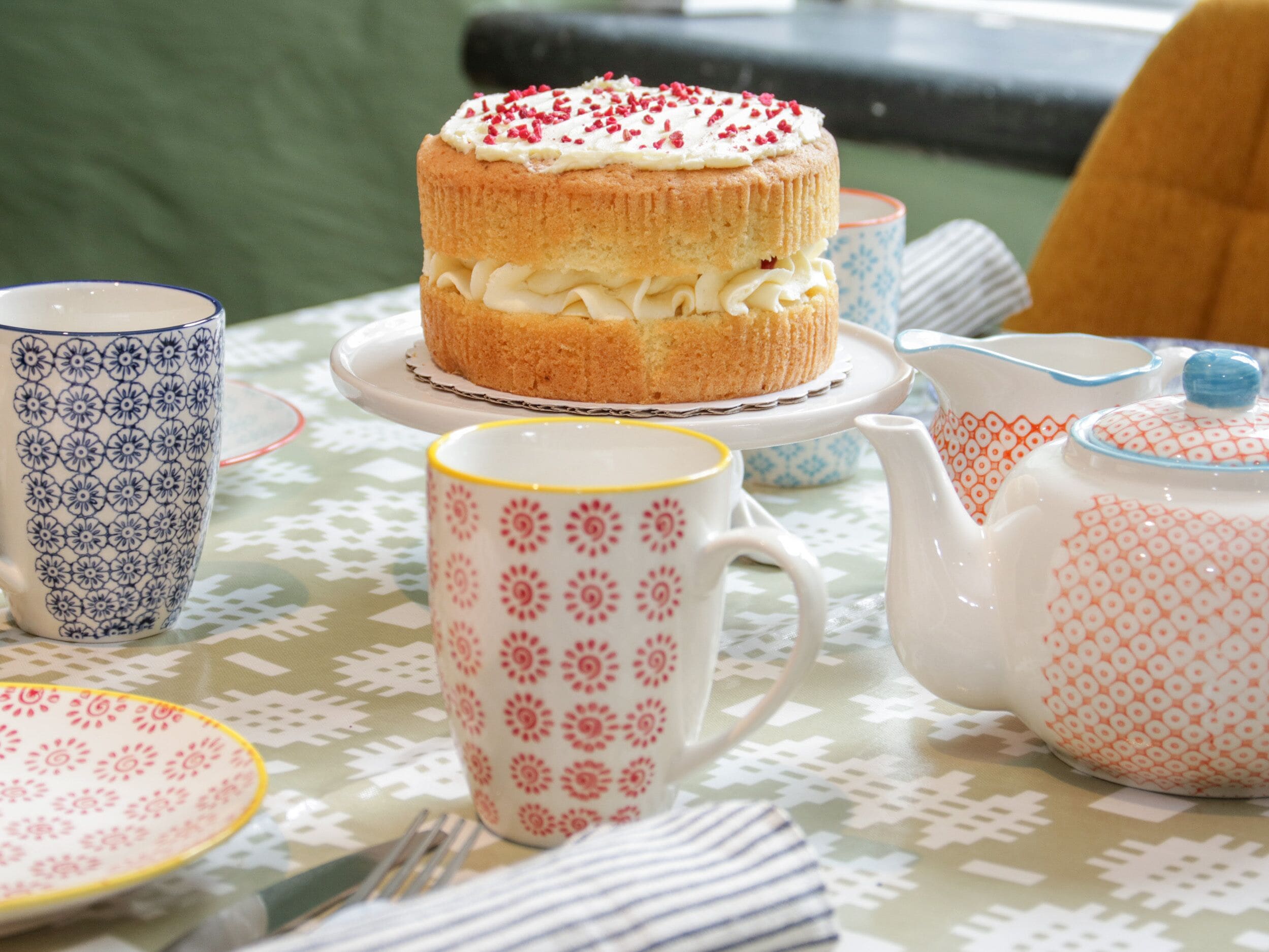 A table with a cake, teapot, cups, and plates.