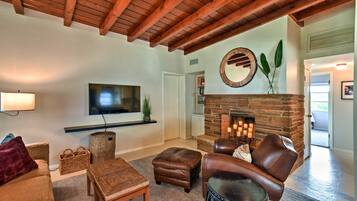 Una sala de estar acogedora con chimenea, muebles de cuero y un televisor instalado en la pared.