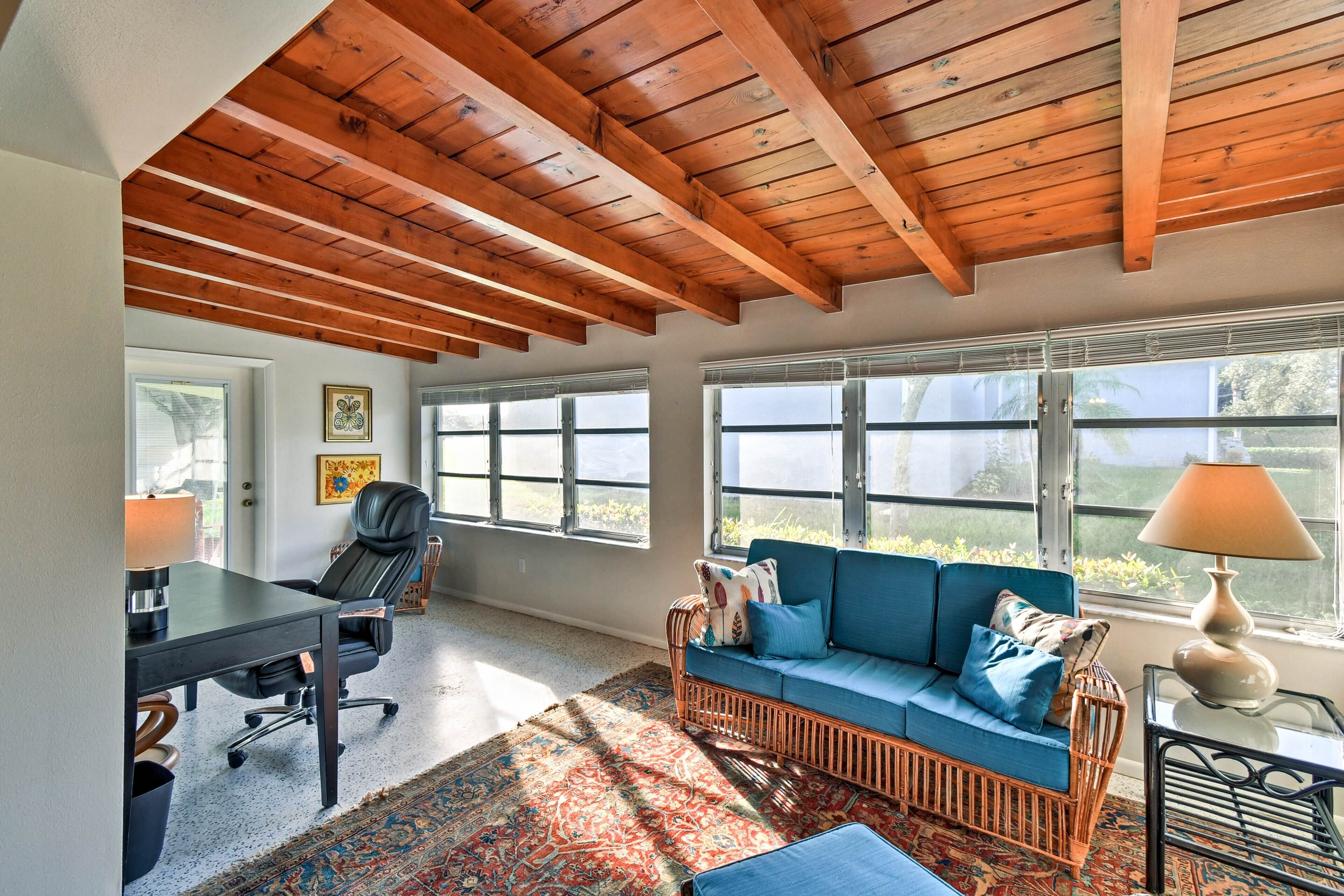 Une pièce avec un plafond en bois, un canapé bleu, un bureau avec une chaise et de grandes fenêtres.