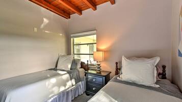Un dormitorio con dos camas individuales, cabecero de madera, una mesita de noche con lámpara y ventana que proporciona luz natural.