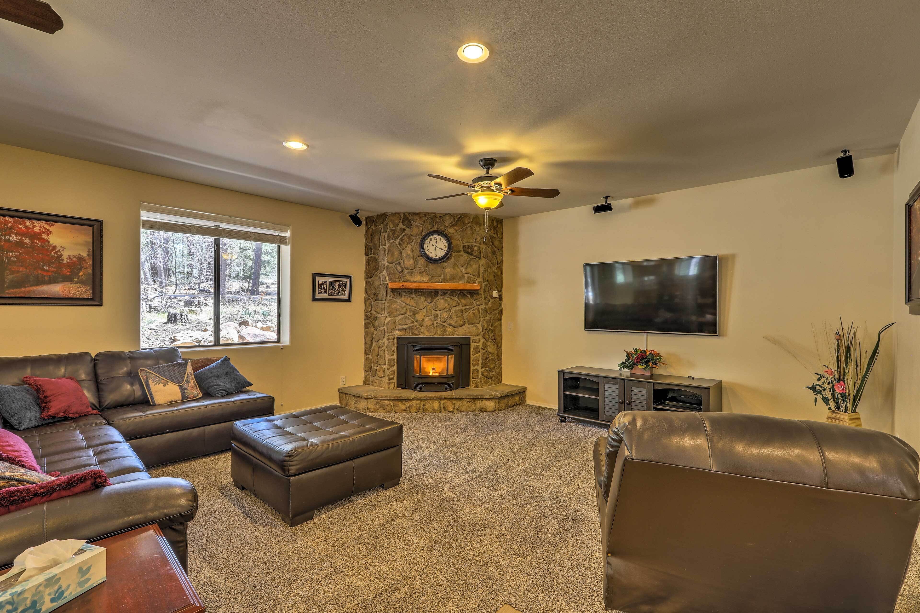 A living room with a stone fireplace, leather sofas, a flat-screen TV, and a ceiling fan.