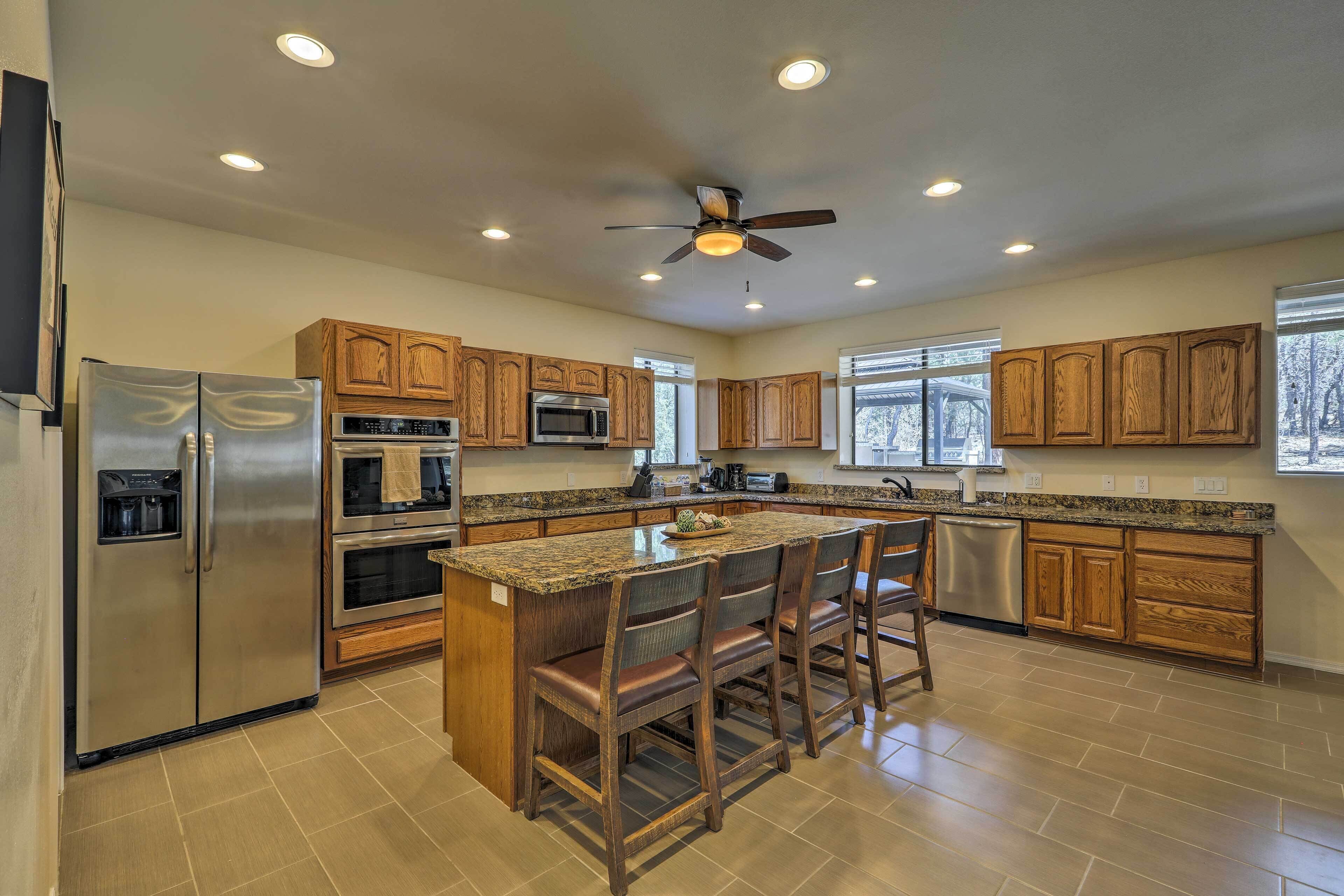 A modern kitchen with wooden cabinets, stainless steel appliances, a central island with bar stools, and a ceiling fan.