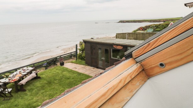 A coastal view with a wooden deck, a small building labeled 'TUB SNACK', and a grassy area with tables set for dining. - On The Watersedge (Chathill)