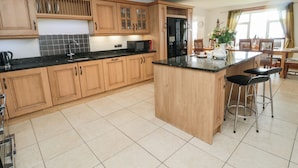 A spacious kitchen with wooden cabinets, a black refrigerator, and a central island with bar stools. - On The Watersedge (Chathill)