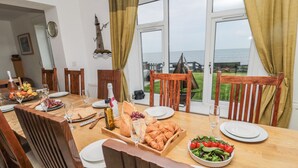 A dining table set for a meal with various dishes, a bottle of wine, and a view of the sea through large windows. - On The Watersedge (Chathill)