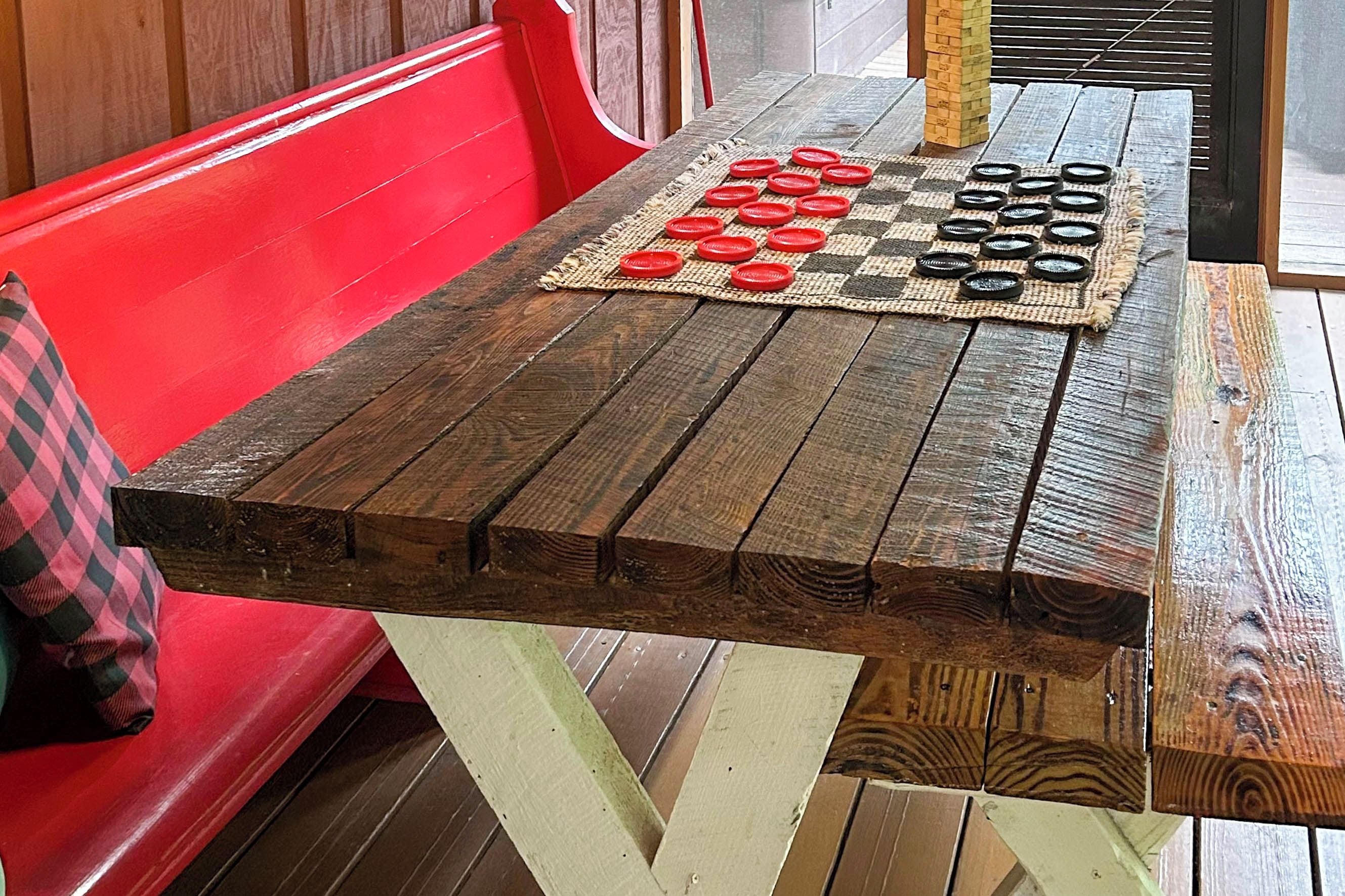 Una mesa de madera con un mantel a cuadros, un banco rojo y un posavasos tejido con fichas de juego.