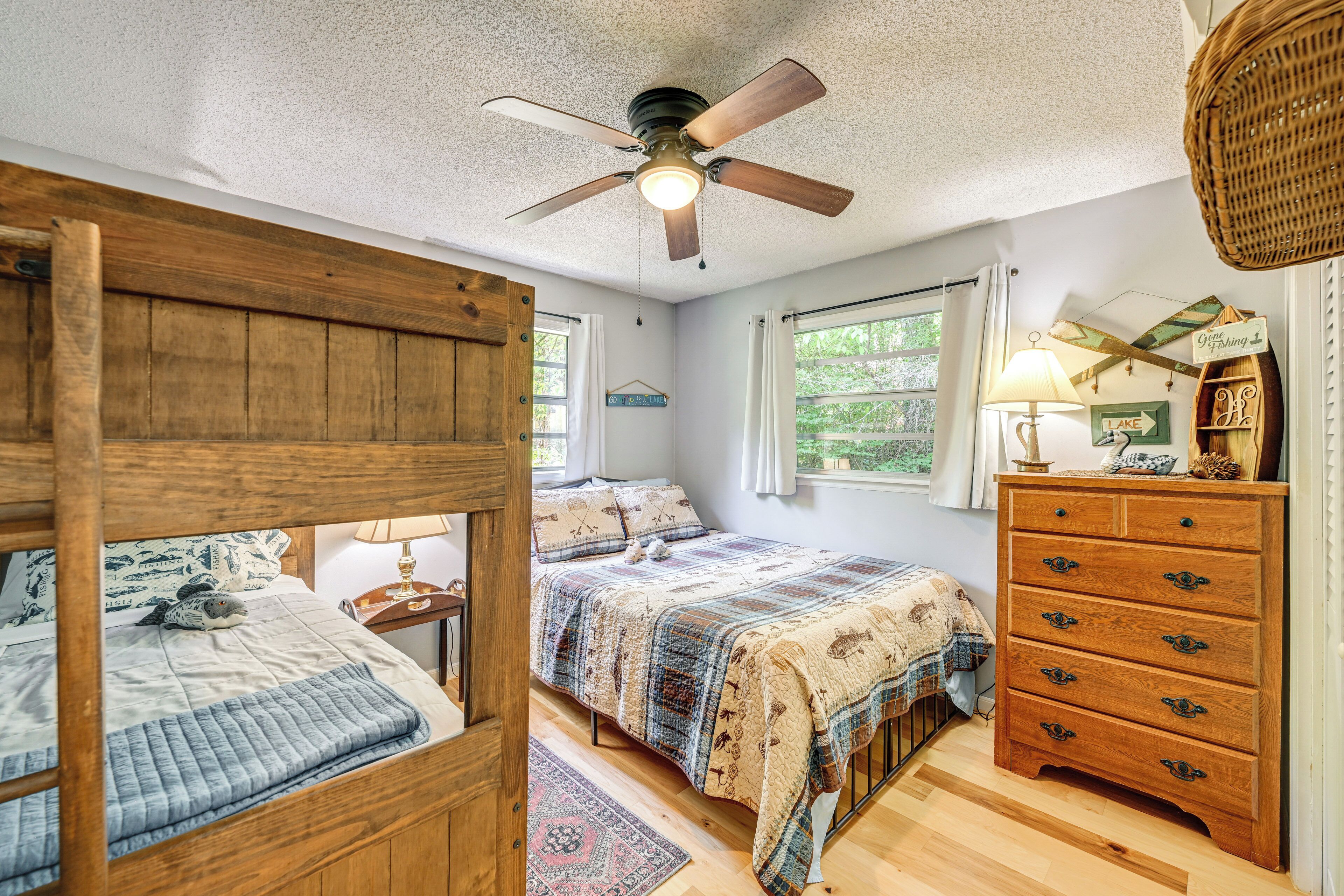 A bedroom with a bunk bed, a double bed, a dresser, a ceiling fan, and a window with curtains.