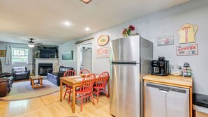 A compact kitchen with a stainless steel refrigerator, a dishwasher, and a coffee maker. There is a dining table with red chairs and a rug on the floor.