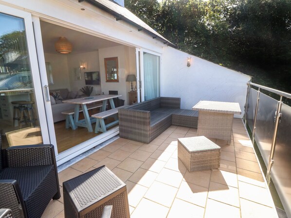 An outdoor patio with wicker furniture, a sliding glass door leading to a living area, and a metal railing.