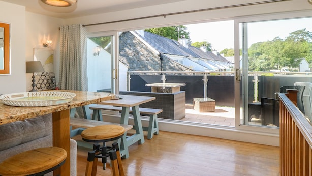 En rymlig balkong med ett träbord och stolar, en soffa i rotting och utsikt över ett bostadsområde.