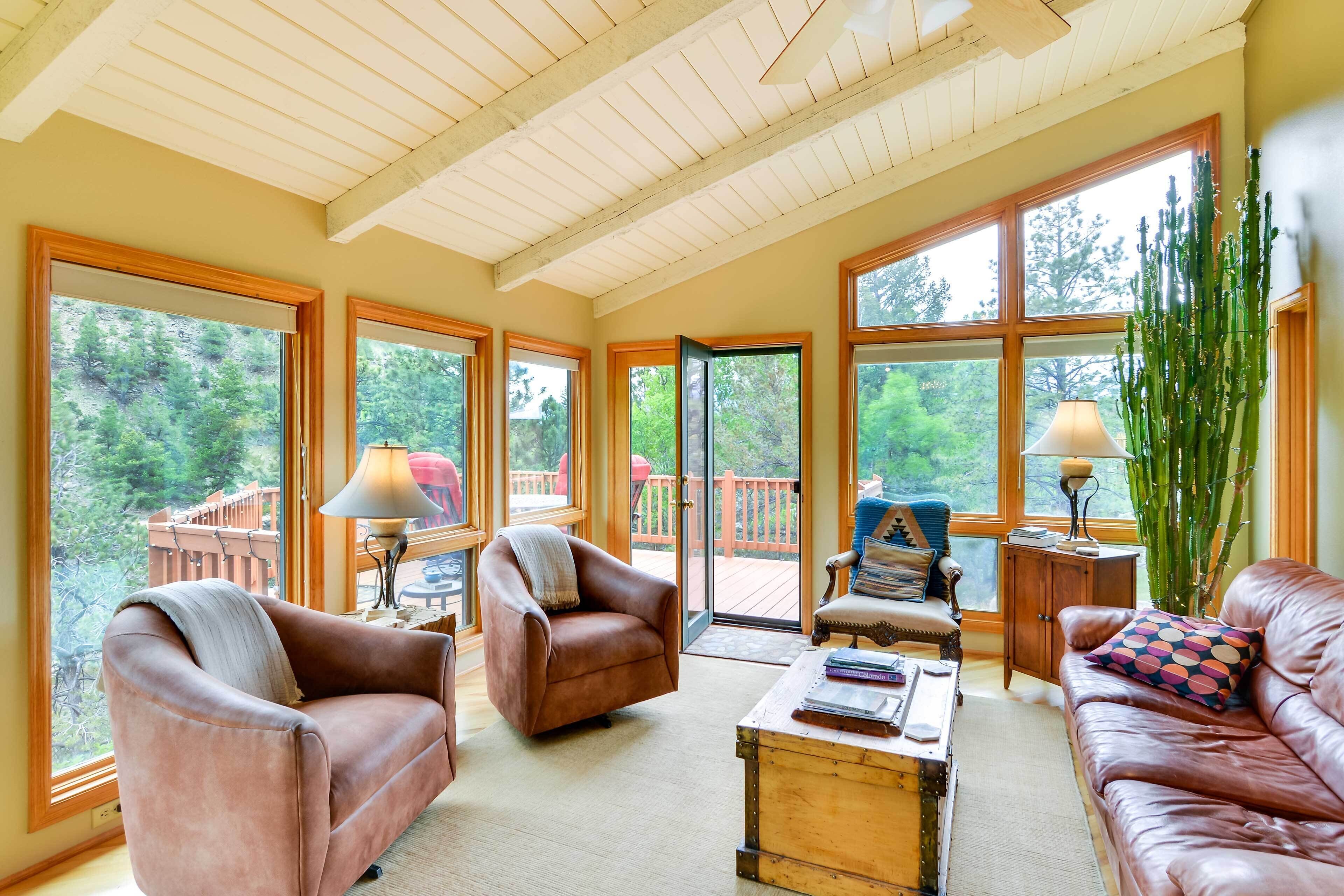 A spacious sunroom with large windows, leather sofas, and a wooden coffee table.