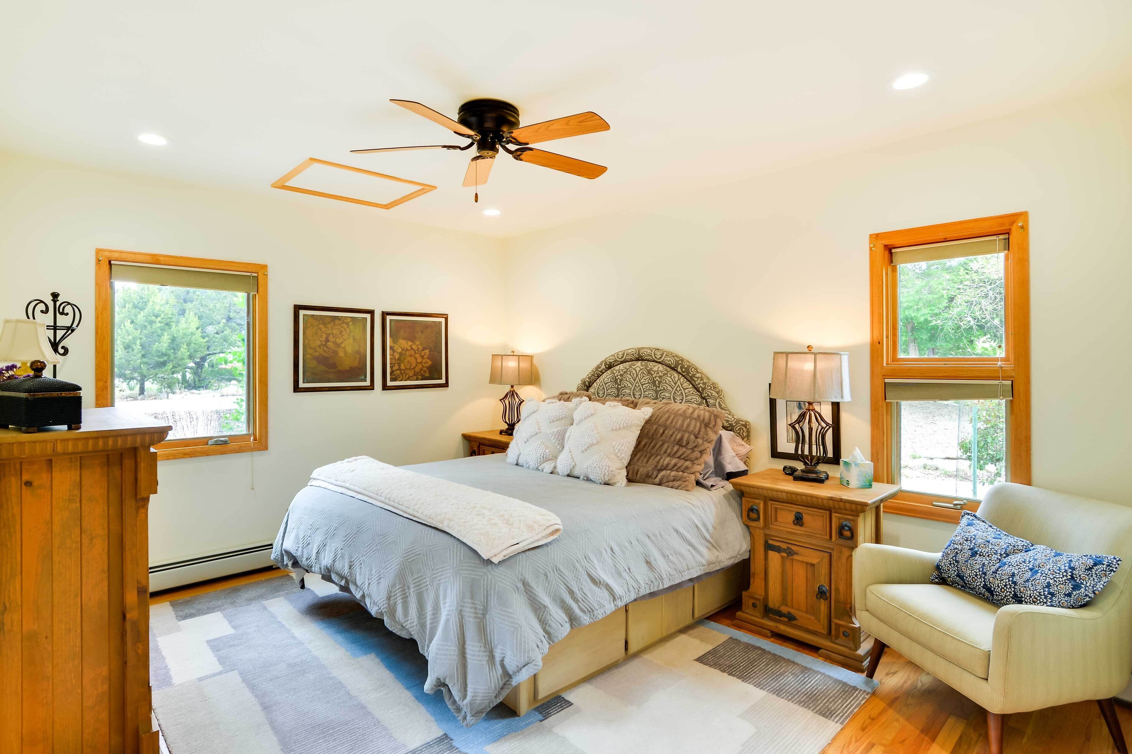 A bedroom with a bed, nightstands, a chair, a ceiling fan, and windows.