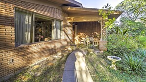 A modern house with a brick exterior, a covered patio, and a garden with plants and a bird bath. - Mid-century Hideaway: Spacious Brownsville Home! (Brownsville)
